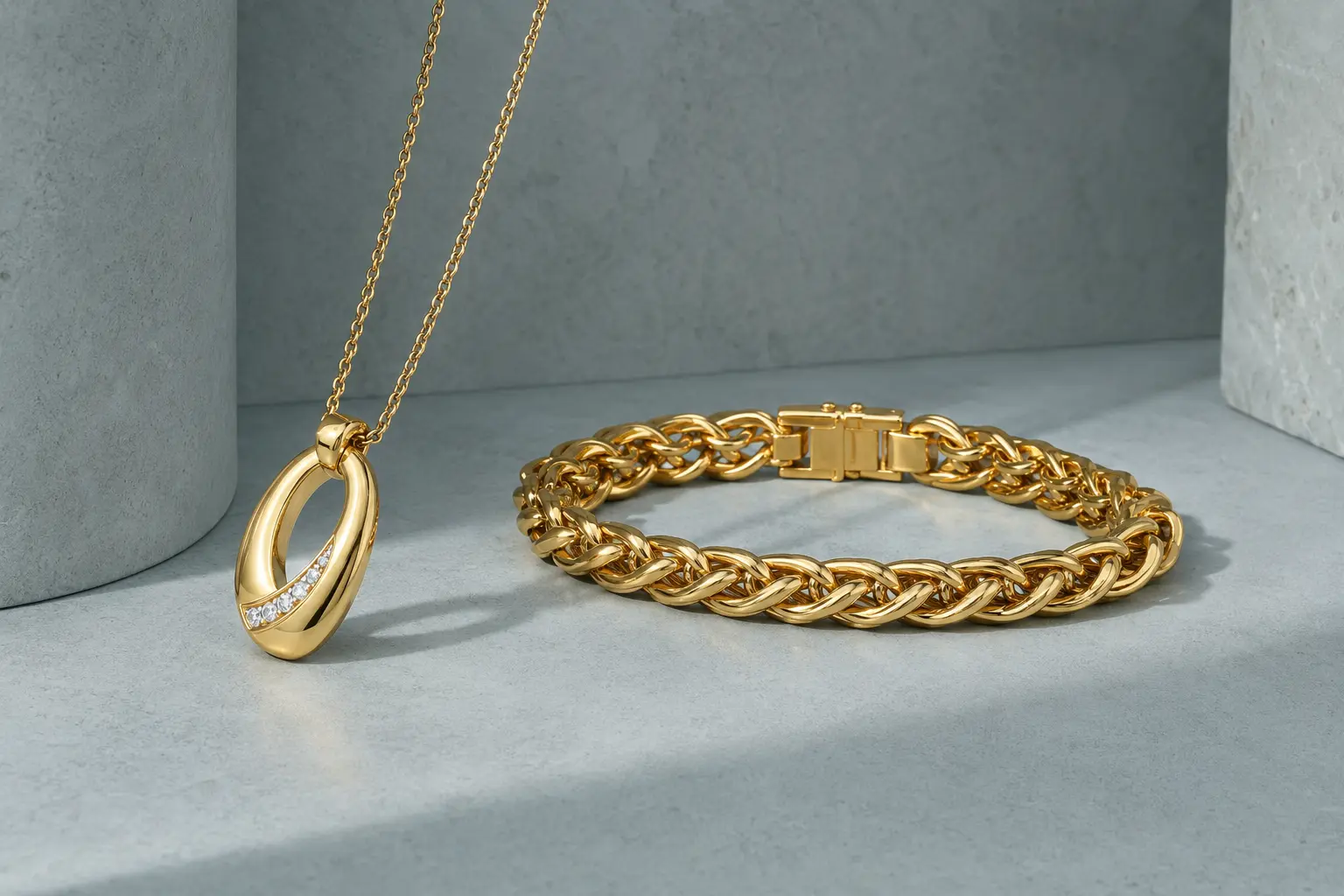 Gold pendant and bracelet presented on a cool celadon architectural surface